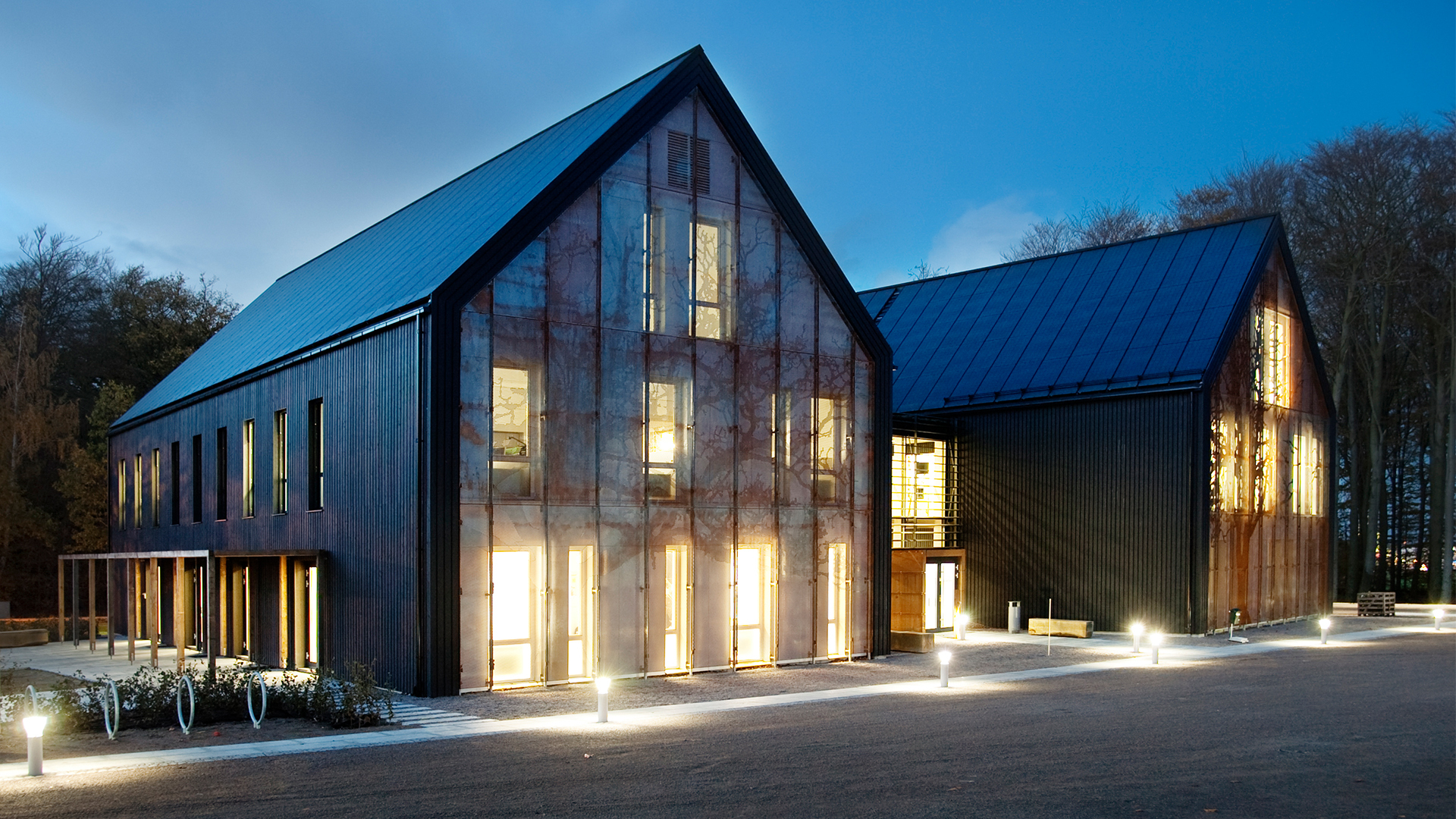 Väla Gård office building exterior at dusk with illuminated windows and black wooden facade.